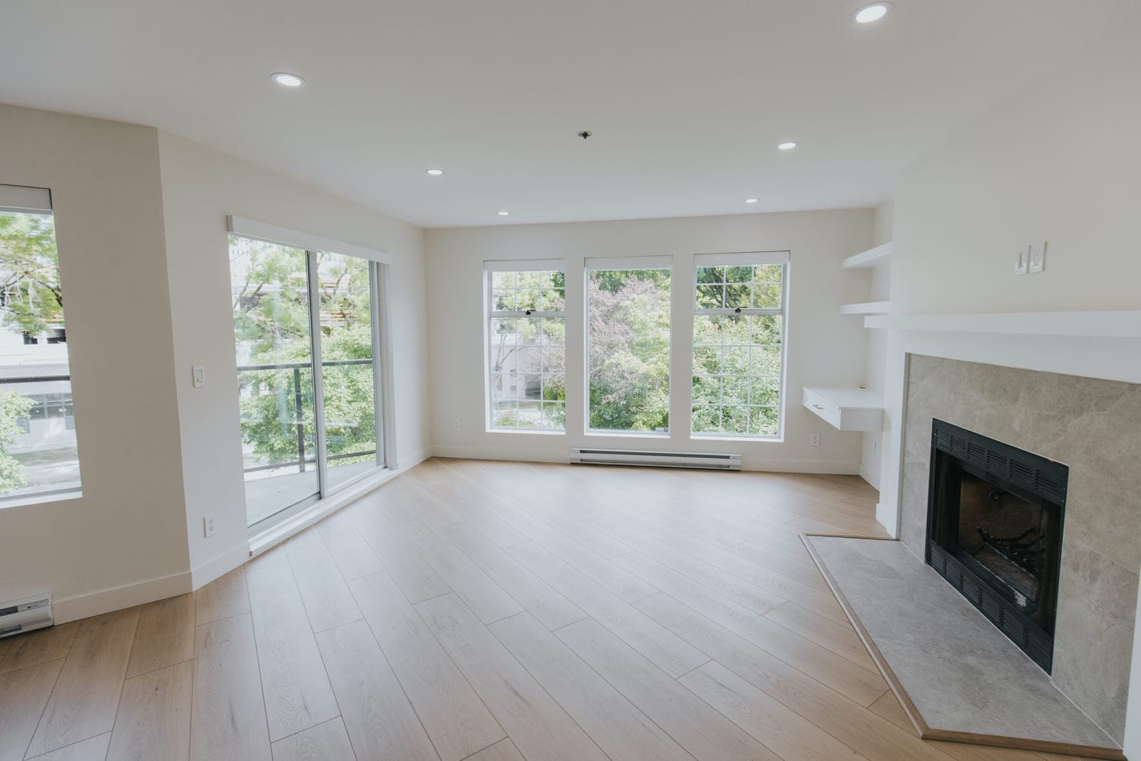 Renovated living room in a Fairview condo with new wide-plank luxury vinyl flooring, pot lighting, rebuilt fireplace surround, and built-in desk and shelving