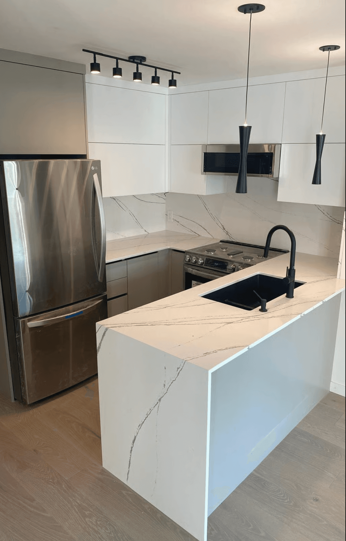 Renovated kitchen in a Yaletown condo with flat-panel white cabinetry, waterfall quartz counters with soft veining, and matte black fixtures