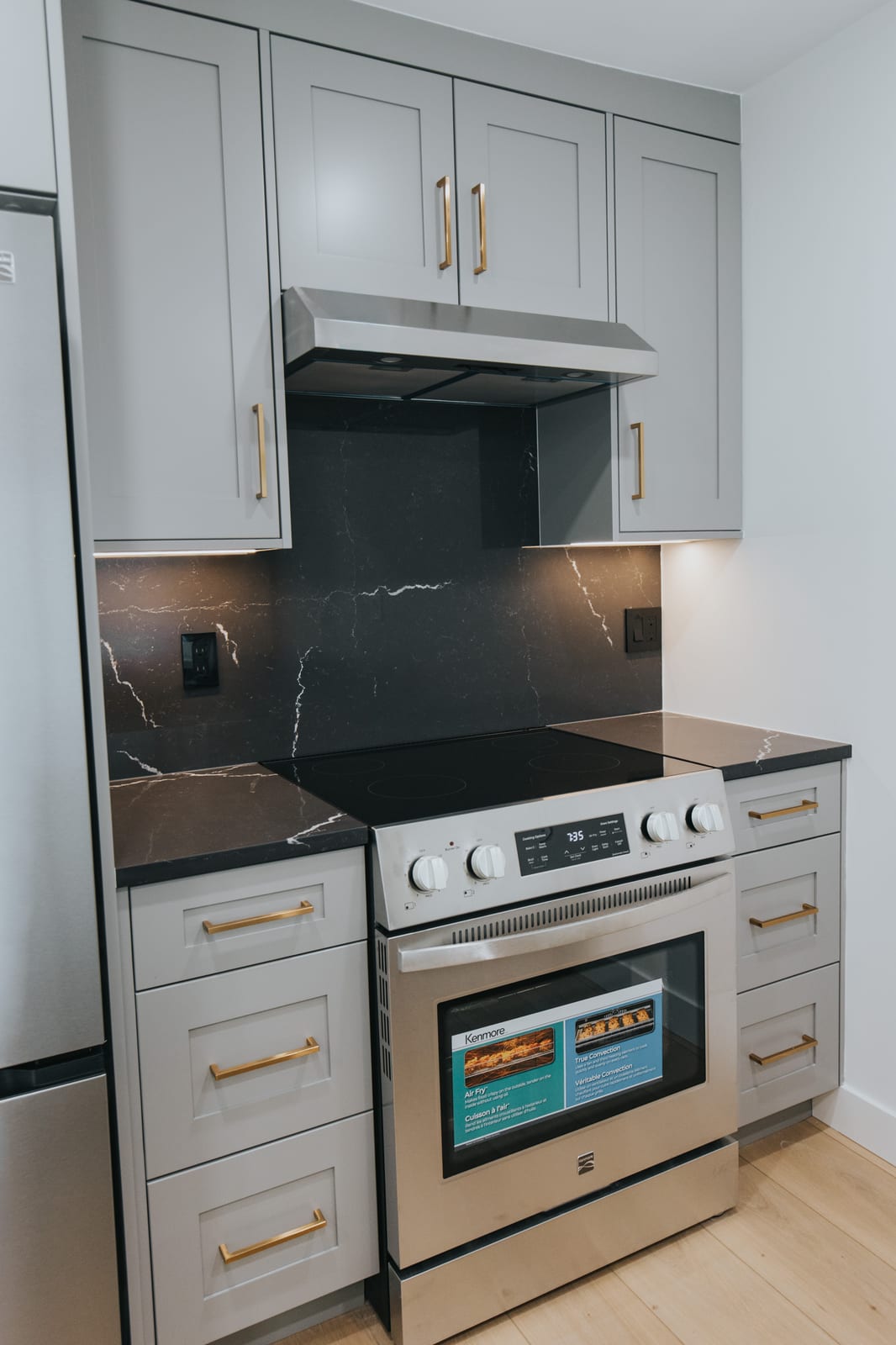 Kitchen range wall with black quartz backsplash, stainless hood, and brushed gold pulls