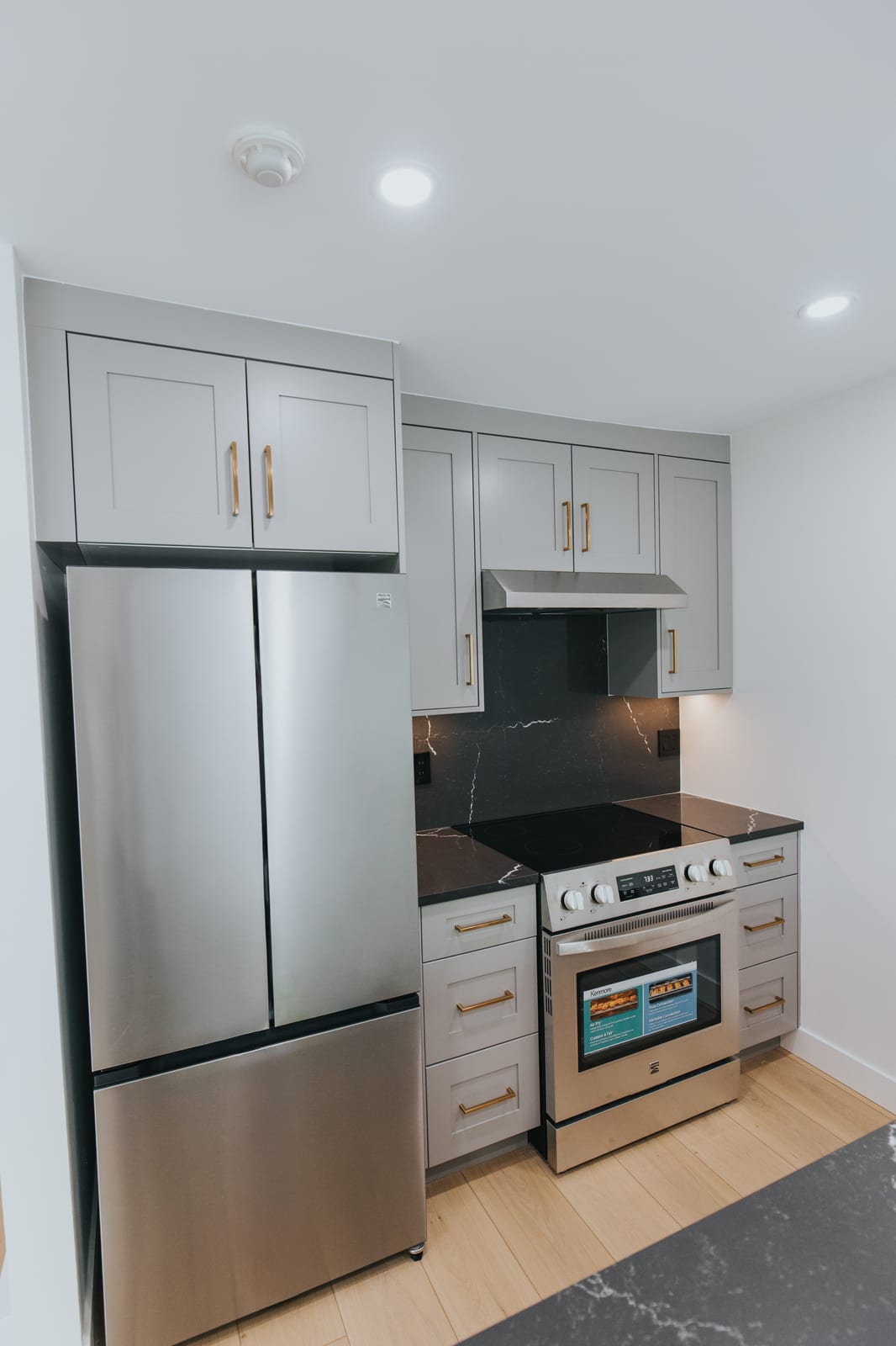 Renovated kitchen with grey shaker cabinetry, black quartz counters and backsplash, and brushed gold hardware